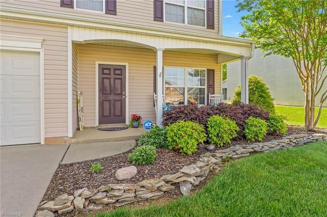 view of exterior entry featuring a yard, a garage, and covered porch