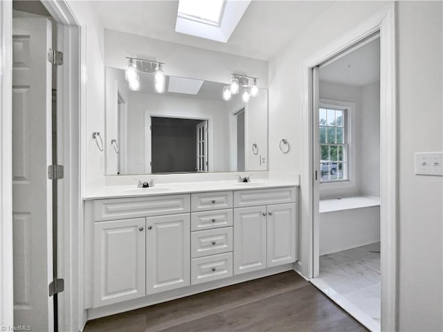 full bath with a skylight, double vanity, and wood finished floors