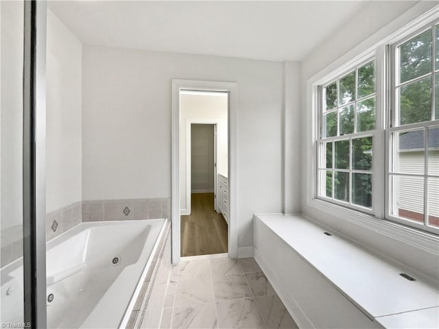 full bath featuring plenty of natural light, marble finish floors, and a jetted tub