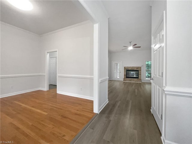 unfurnished living room with a ceiling fan, dark wood finished floors, ornamental molding, baseboards, and a fireplace