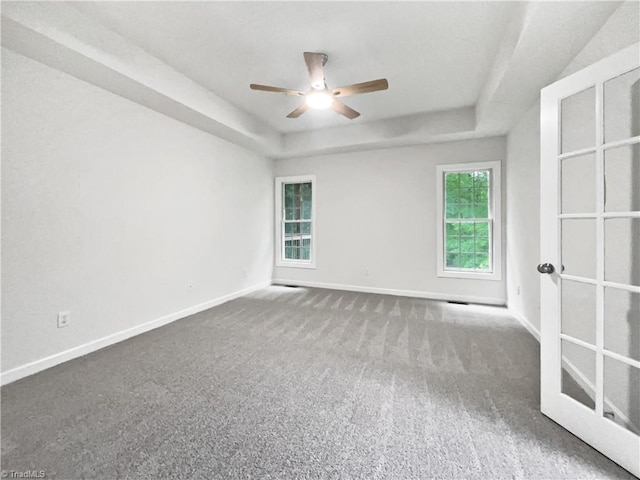 empty room featuring a raised ceiling, a ceiling fan, baseboards, and carpet