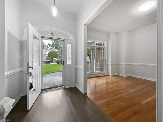 foyer entrance with wood finished floors, ornamental molding, and baseboards