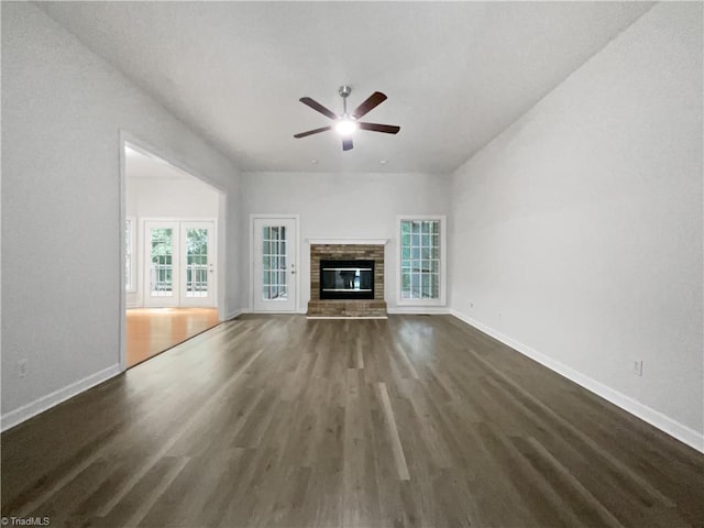 unfurnished living room featuring wood finished floors, ceiling fan, baseboards, and a brick fireplace