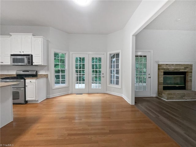 kitchen with appliances with stainless steel finishes, white cabinets, light wood-type flooring, open floor plan, and plenty of natural light
