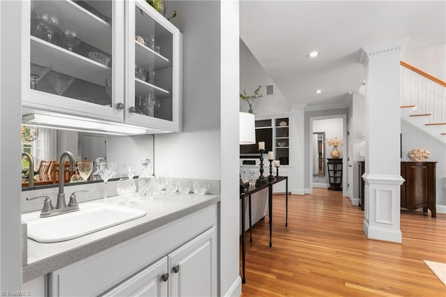 bar with white cabinets, light hardwood / wood-style floors, ornate columns, and sink