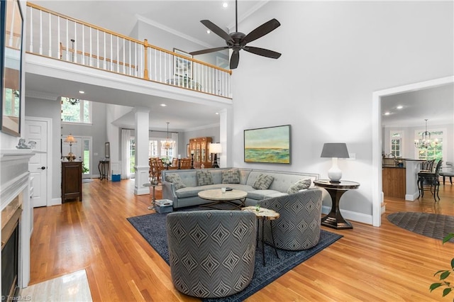 living room featuring crown molding, light hardwood / wood-style flooring, a towering ceiling, and ceiling fan with notable chandelier