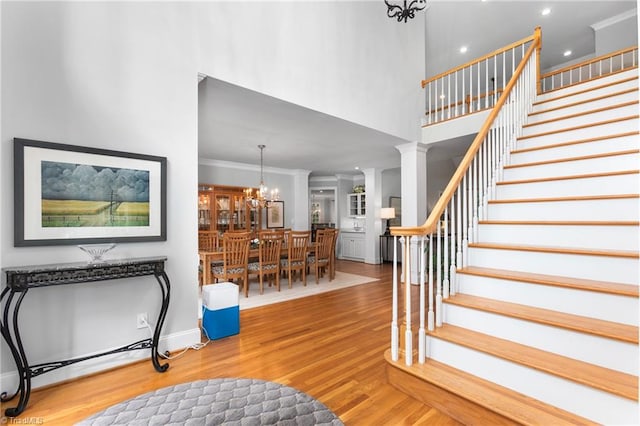 foyer featuring decorative columns, ornamental molding, a high ceiling, an inviting chandelier, and hardwood / wood-style floors