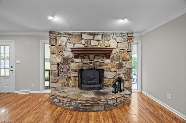 interior details with a stone fireplace, visible vents, wood finished floors, baseboards, and ornamental molding