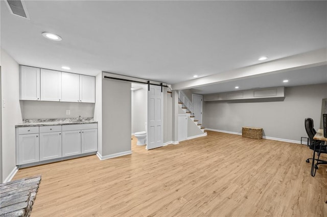 finished basement with a barn door, a sink, light wood-style floors, recessed lighting, and baseboards