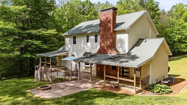 back of house with a chimney, roof with shingles, a patio area, an outdoor fire pit, and a yard