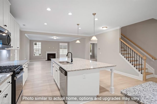 kitchen with white cabinets, appliances with stainless steel finishes, light stone counters, and a kitchen island with sink