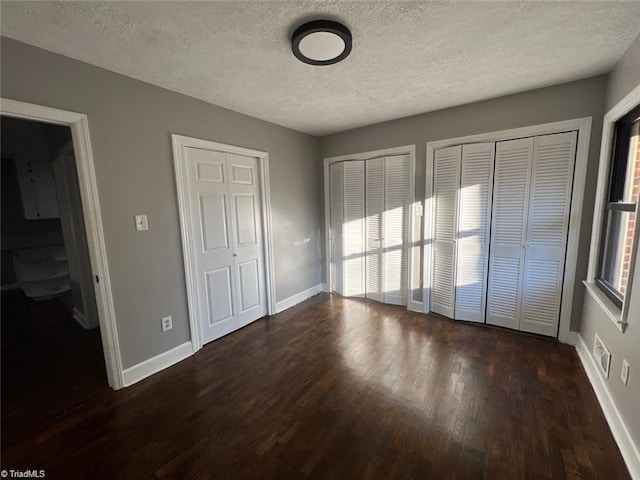 unfurnished bedroom featuring multiple closets, a textured ceiling, and dark hardwood / wood-style floors