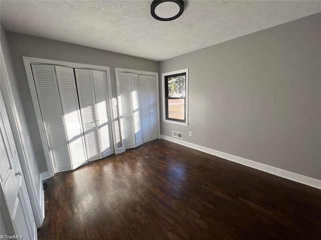 unfurnished bedroom with a textured ceiling, multiple closets, and dark wood-type flooring