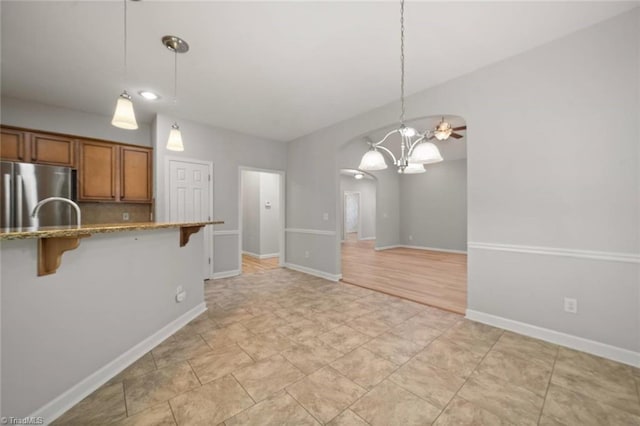 kitchen featuring brown cabinets, hanging light fixtures, stainless steel refrigerator, a breakfast bar area, and arched walkways