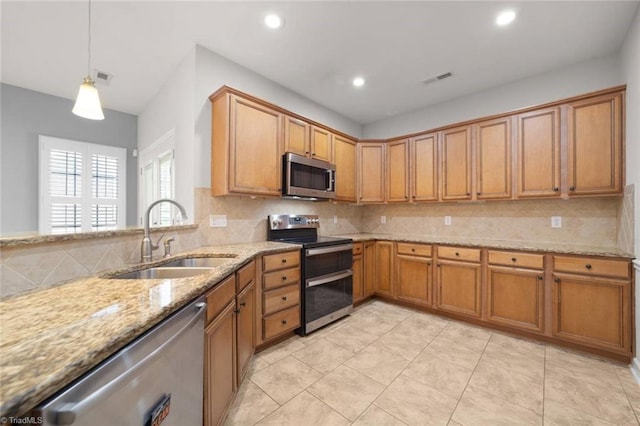 kitchen with brown cabinets, light stone counters, a sink, stainless steel appliances, and decorative backsplash