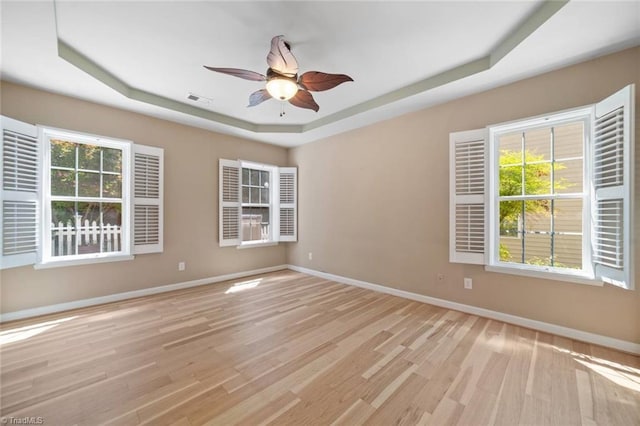 unfurnished room featuring baseboards, a ceiling fan, a tray ceiling, and light wood finished floors