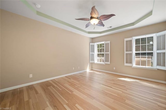 spare room featuring a ceiling fan, visible vents, baseboards, light wood finished floors, and a tray ceiling