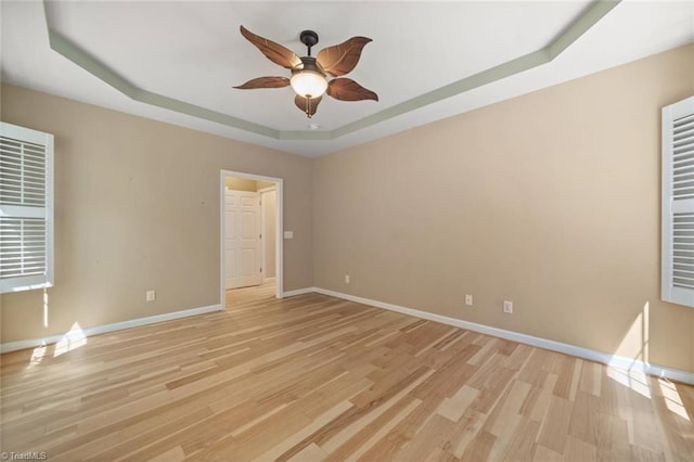 spare room featuring a raised ceiling, baseboards, a ceiling fan, and light wood finished floors