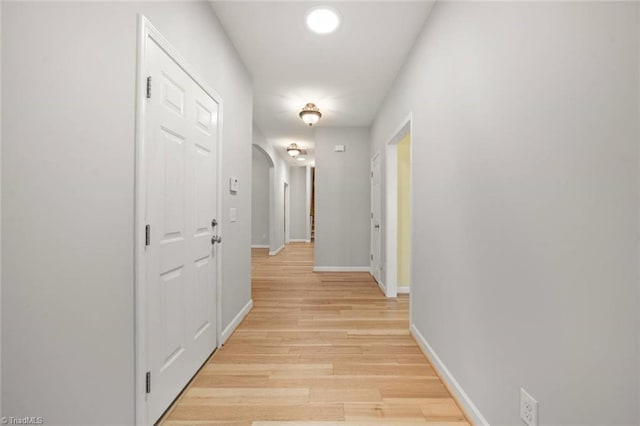 hall featuring arched walkways, baseboards, and light wood-type flooring