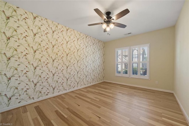 empty room with visible vents, wood finished floors, baseboards, wallpapered walls, and a ceiling fan