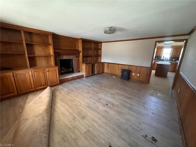 unfurnished living room with light wood-style flooring, ornamental molding, wooden walls, wainscoting, and a brick fireplace