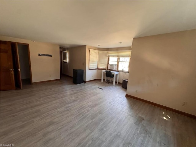 unfurnished living room with cooling unit, baseboards, and wood finished floors