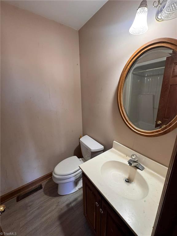 full bathroom featuring vanity, wood finished floors, visible vents, baseboards, and toilet