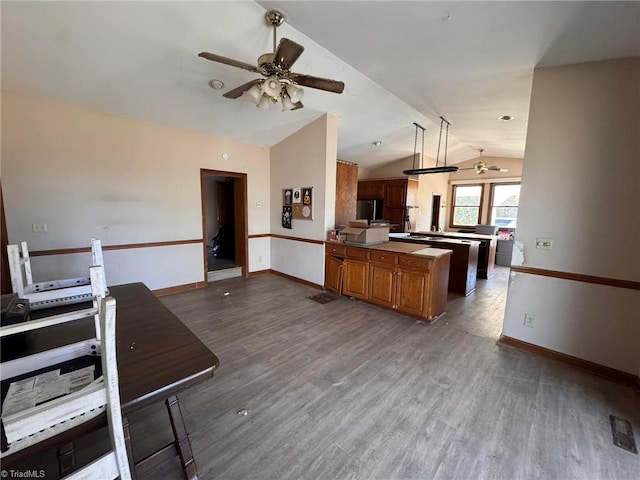 kitchen with a ceiling fan, dark wood-type flooring, brown cabinetry, and vaulted ceiling