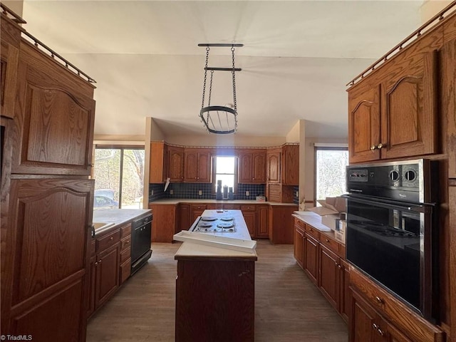 kitchen featuring backsplash, a center island, brown cabinets, dark wood-style floors, and black appliances