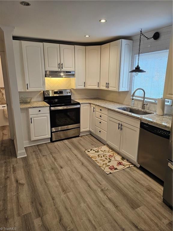 kitchen with under cabinet range hood, appliances with stainless steel finishes, light wood-style floors, white cabinetry, and a sink