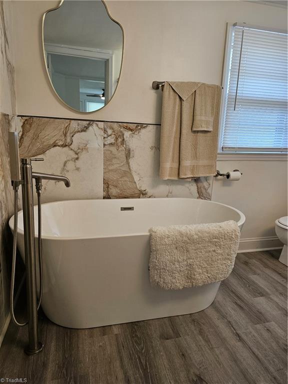 bathroom with toilet, a freestanding bath, baseboards, and wood finished floors