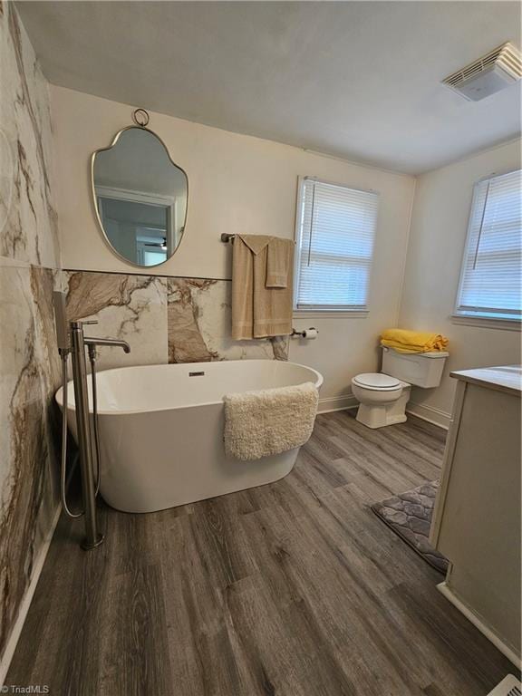 bathroom featuring visible vents, toilet, wood finished floors, a soaking tub, and vanity