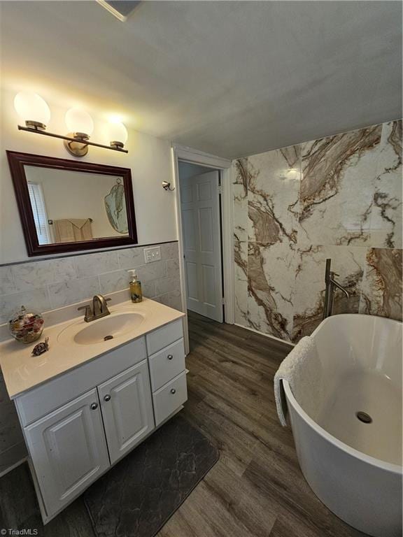 full bathroom with vanity, tile walls, a freestanding tub, and wood finished floors