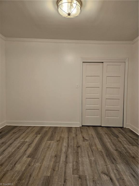 unfurnished bedroom featuring a closet, dark wood-type flooring, baseboards, and ornamental molding