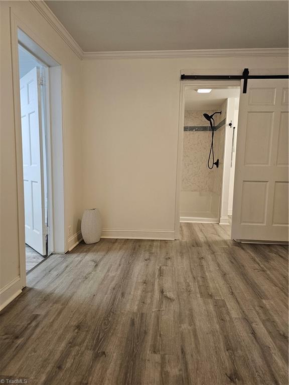 spare room featuring a barn door, wood finished floors, baseboards, and ornamental molding