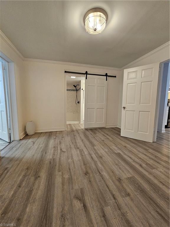 empty room with baseboards, crown molding, a barn door, and wood finished floors