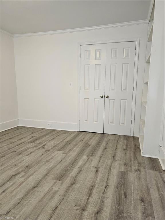 unfurnished bedroom featuring crown molding, wood finished floors, a closet, and baseboards