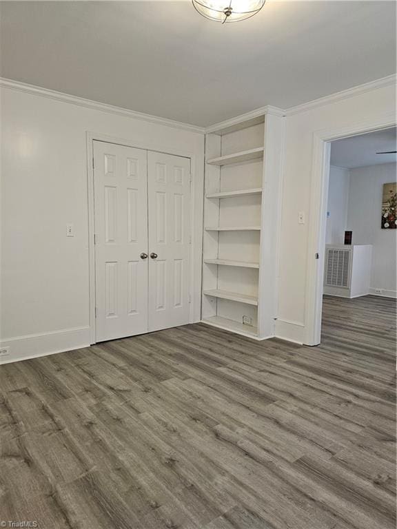 unfurnished bedroom featuring a closet, baseboards, wood finished floors, and crown molding