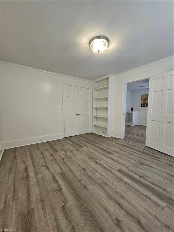 unfurnished bedroom featuring crown molding, wood finished floors, a closet, and baseboards