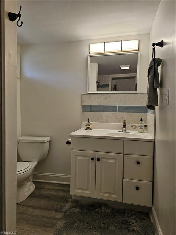 bathroom with tasteful backsplash, baseboards, toilet, wood finished floors, and vanity