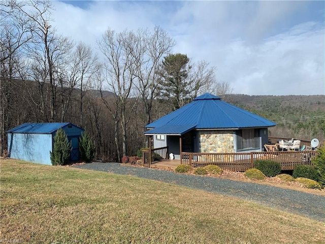 exterior space with a deck, a shed, a forest view, gravel driveway, and an outdoor structure