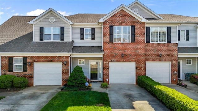 view of property with a shingled roof, an attached garage, driveway, and brick siding