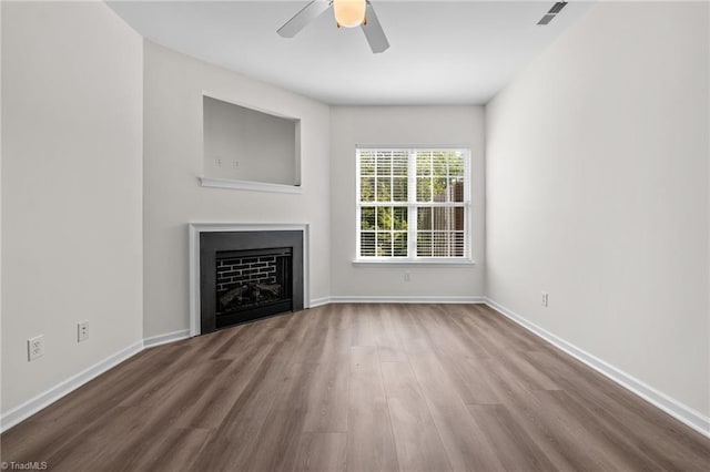 unfurnished living room featuring a ceiling fan, baseboards, wood finished floors, and a fireplace