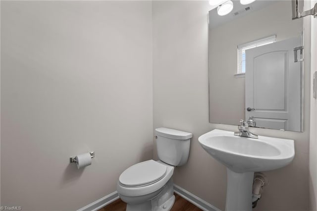 half bathroom featuring toilet, baseboards, visible vents, and wood finished floors