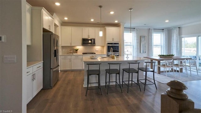 kitchen featuring a center island with sink, white cabinets, pendant lighting, and appliances with stainless steel finishes