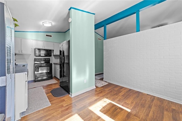 kitchen with white cabinets, light hardwood / wood-style floors, brick wall, and black appliances