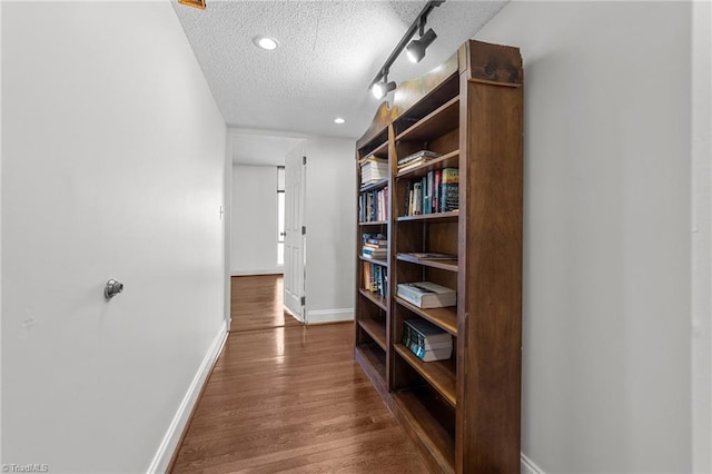 corridor featuring rail lighting, a textured ceiling, and dark wood-type flooring