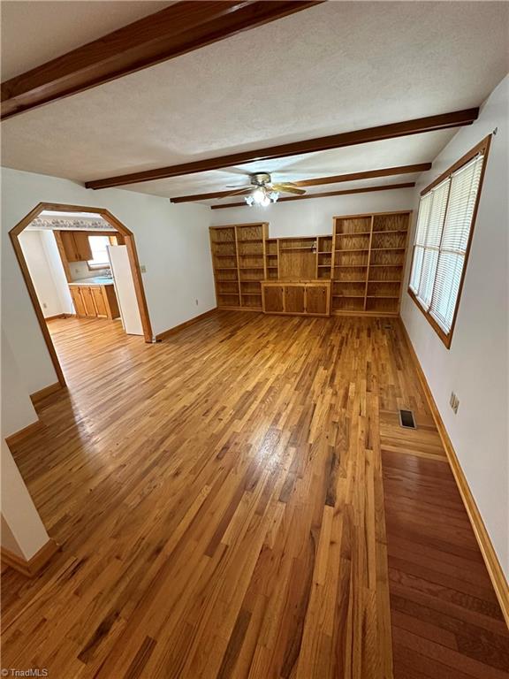 unfurnished living room with a textured ceiling, ceiling fan, light wood-type flooring, and beamed ceiling