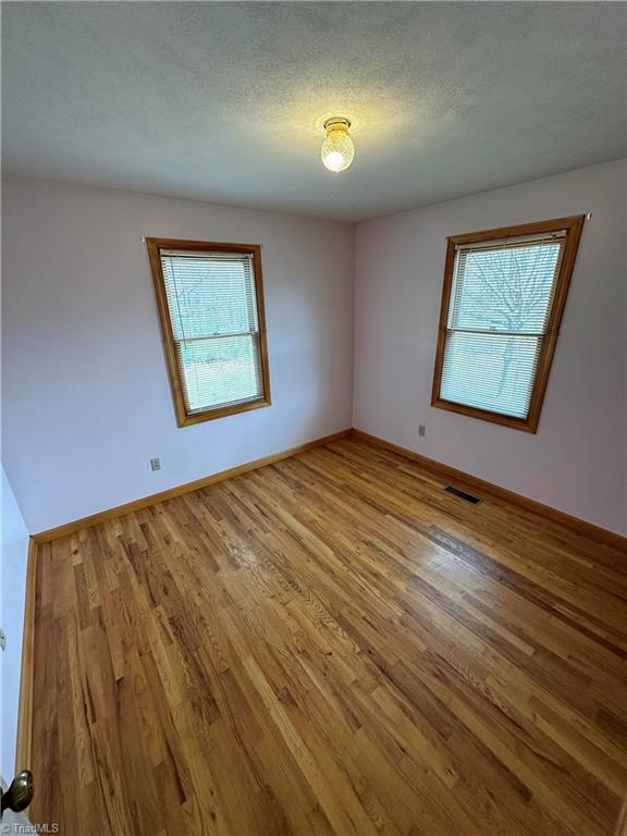 empty room with light hardwood / wood-style floors and a textured ceiling