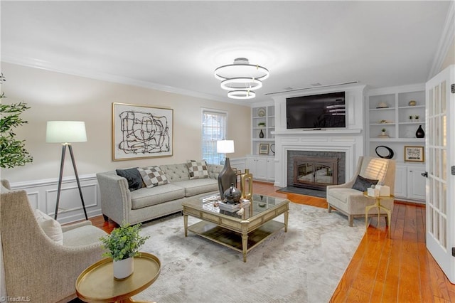 living room featuring wood-type flooring, a brick fireplace, built in shelves, and crown molding